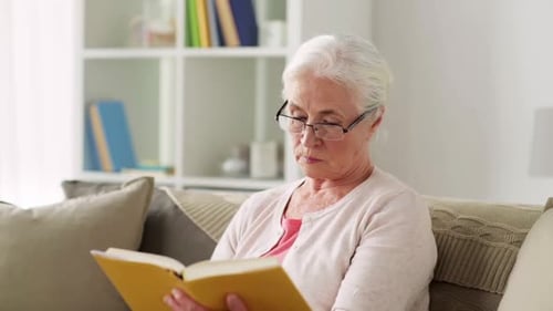 Senior woman enjoys relaxing at home reading a book with eyeglasses on