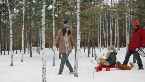 Cheerful Family with Sled and Bags Walking in Snow at Forest Vacation Village