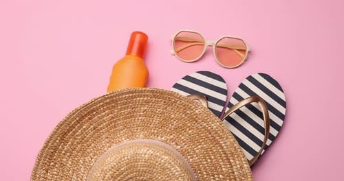 Strohhut, Flip-Flops, Sonnenbrille und Sonnencreme auf rosafarbenem Hintergrund, flach liegend