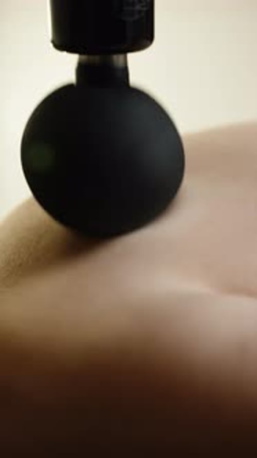 Closeup of a Percussive Massage Device with a Round Ball Attachment Pressing Into Back Muscles