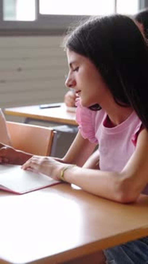 Primary School Children Concentrate on Writing in Notebooks While Sitting at Desk in Class