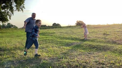 Grandfather and Children Play on Grassy Field at Sunset