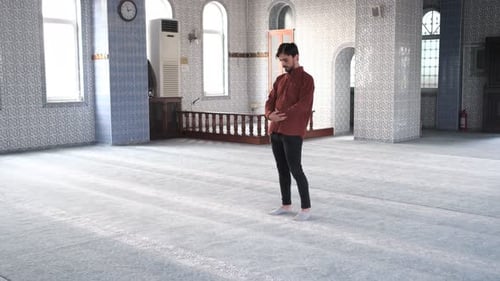 Vorderansicht eines Mannes, der in der Moschee steht und sich zum Beten niederwirft, ein junger erwachsener kaukasischer Mann betet