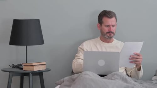 Man Works on Laptop in Bed at Home