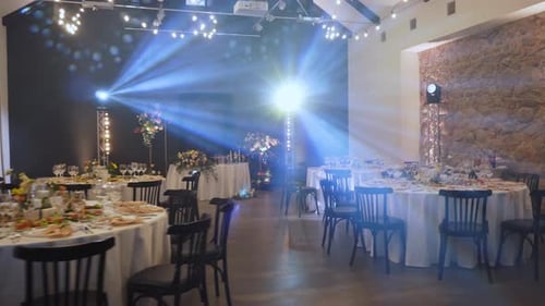 Dark Banquet Hall with Flower Decorated Round Tables and Stage Lighting