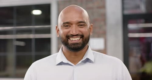 Portrait of happy biracial bald creative businessman with beard smiling in office, in slow motion