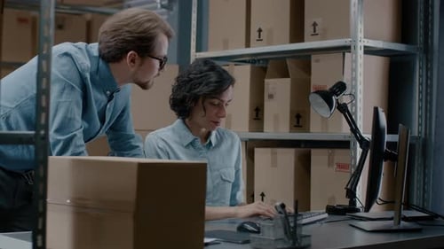 Male and Female Warehouse Inventory Managers Talking, Using Personal Computer and Checking Stock. I