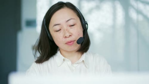 Close up. Asian woman in a headset customer service operator talking on a video call while sitting