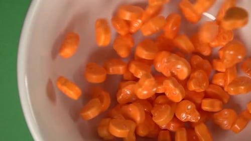 Close up of orange skulls and bones shaped candy falling on a plate, on a chroma background.