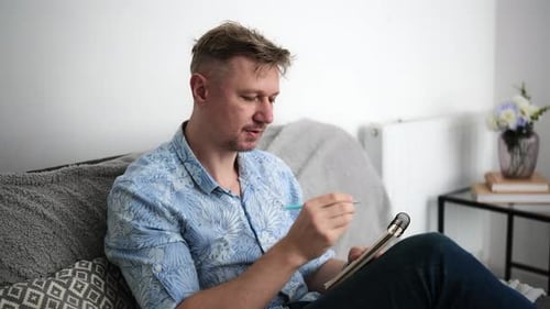 Man Writing in Notebook While Sitting on Couch
