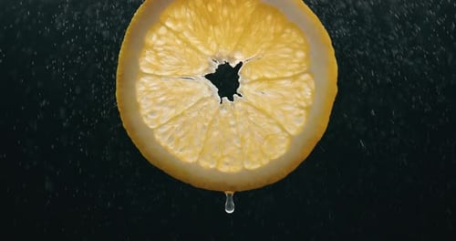 Fresh Orange Slice Splashed by Water Tröpfchennebel mit Flüssigkeitstropfen in Zeitlupe, hintergrundbeleuchteter schwarzer Hintergrund