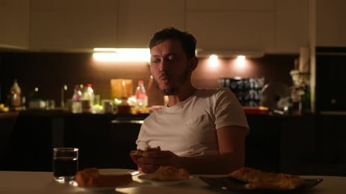 Front View of Calm Hungry Young Man Eating Hamburger and Drinking Unhealthy Beverage Sitting Alone