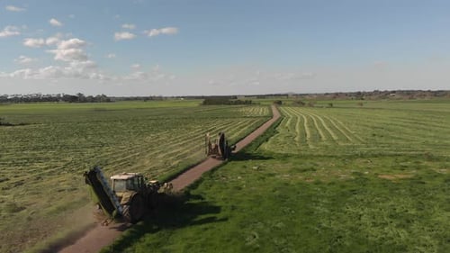 Aerial footage following two tractor mowers from the side. Travelling down gravel road.