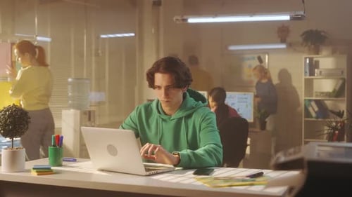 A Young Man is Typing on a Laptop Keyboard While Sitting at a Table in the Office