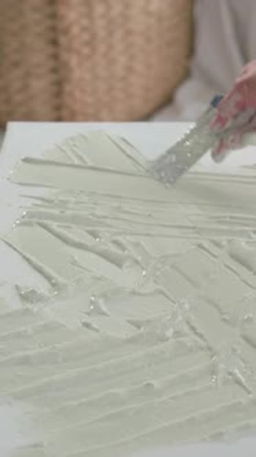 Woman spreading off-white gel, scraping with metal spatula and refining ridged texture for art