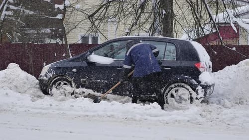 Man Shoveling Snow Around Black Car in Winter