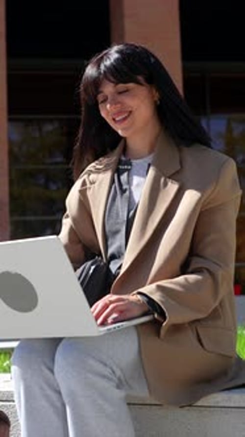 Young female university student working on laptop outdoors