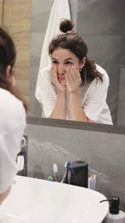 Woman Washing and Drying Face in Bathroom Mirror