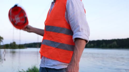 Male Engineer Holding Helmet Posing Outdoors with Beautiful River on the Background Cropped Close Up