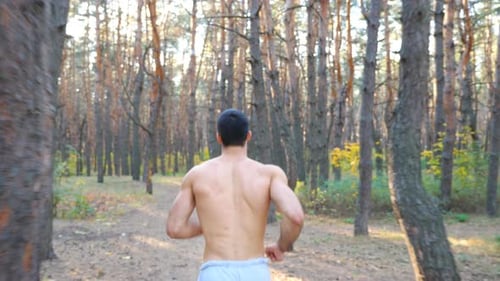 Strong and Muscular Man Running Along Forest Path