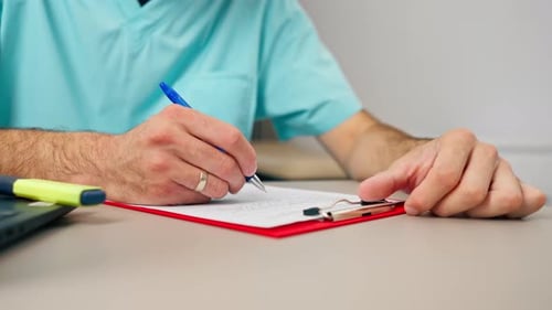 Close-up shot of a male doctor's hand with ring on his finger filling out a patient's medical