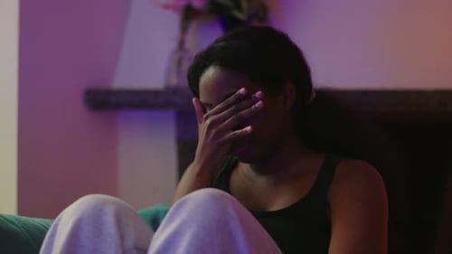 African American woman sitting on couch looking upward with pained expression reflecting despair