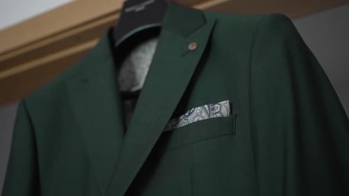 Close-up of a green suit jacket with a patterned pocket square, hanging on a hanger