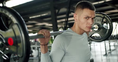 Athletic Man Hold Heavy Barbell on Shoulders and Looking at Camera at Gym