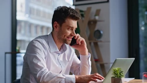 Man in White Shirt Using Laptop and Phone