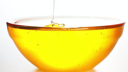 Honey pours into a transparent bowl on white background.