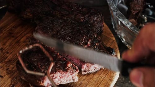 Close-up of a man's hand carving a grilled steak on a rustic wooden cutting board