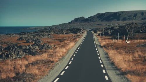 A narrow asphalt road leading through the desolate tundra landscape along the coastline. Pan forward