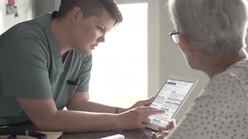 Female healthcare provider showing tablet to senior woman
