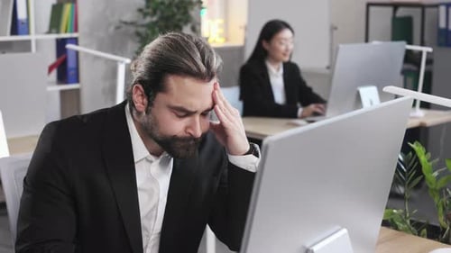 Tired Man Sitting at Office Desk and Suffering From Headache