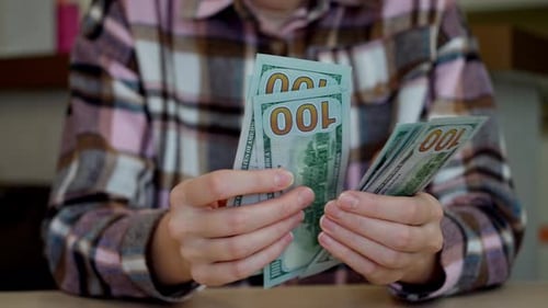 Close-up of a young woman sitting at a table and counting dollar bills