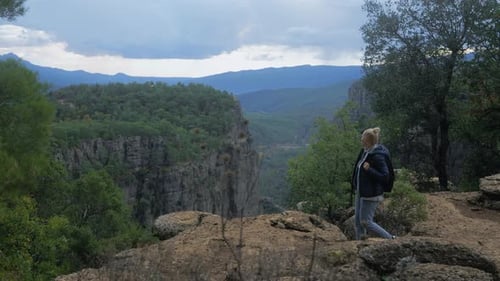 Junge erwachsene Frau mit Rucksack geht auf dem Klippenkamm über dem Canyon spazieren