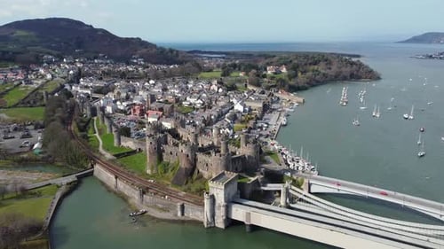 An wider aerial view of Conwy Castle on a sunny day, flying left to right around the castle with the