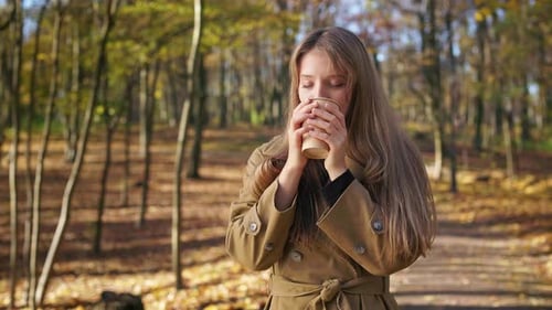 Pretty Young Lady Standing in Park Drinking Coffee with Closed Eyes