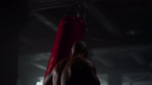 Strong Man Punching Bag in Sport Club at Strength Workout. Silhouette Male