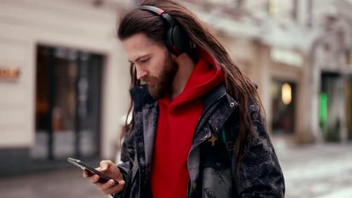 a Stylish Man with Dreadlocks and a Beard Walks Around the City Listening to Music in Wireless