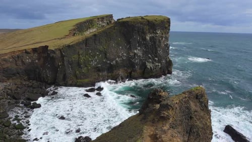 The beautiful Icelandic Valahnúkamöl coastline with rocky cliffs and high waves rolling in from the