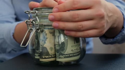 Drehglas zum Geldsparen von weiblichen Händen, gefüllt mit Dollar-Banknoten, Tipps zur Transkription auf der Vorderseite