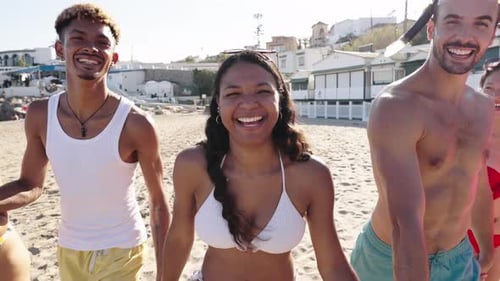Group of Excited Diverse Friends Running Along the Sand in a Urban Beach in Swimwear