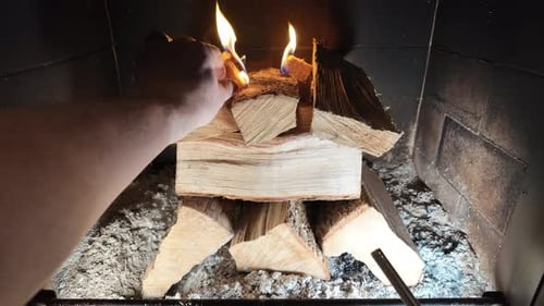 A close-up shot of a hand igniting a natural fire starter with a lighter inside a fireplace filled