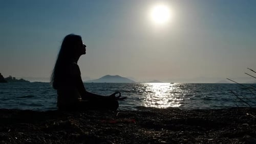 Silhouette of Woman Meditating on Beach at Sunrise