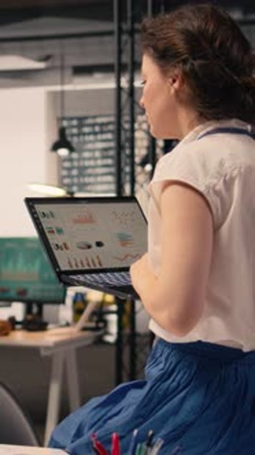 Vertical Video Female Worker Seated on Desk and Working with Laptop in Modern Office