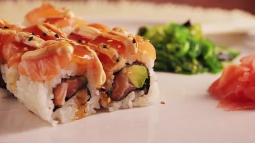 Appetizing sushi rolls with salmon, avocado with special sauce close-up on the table with ginger.