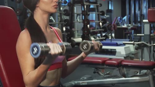 A Determined Girl Passionately Pumps Her Arm Muscles with Heavy Dumbbells