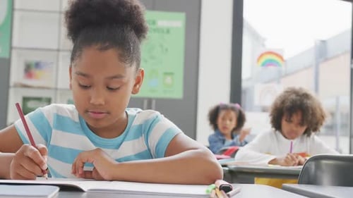 Video of biracial schoolgirl sitting at desk writing in school class