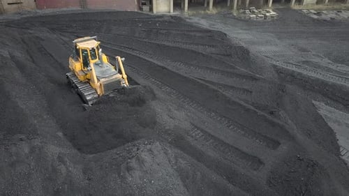 Bulldozer-Traktor sammelt schwarze Kohle auf dem Versorgungsfeld des thermoelektrischen Kraftwerks